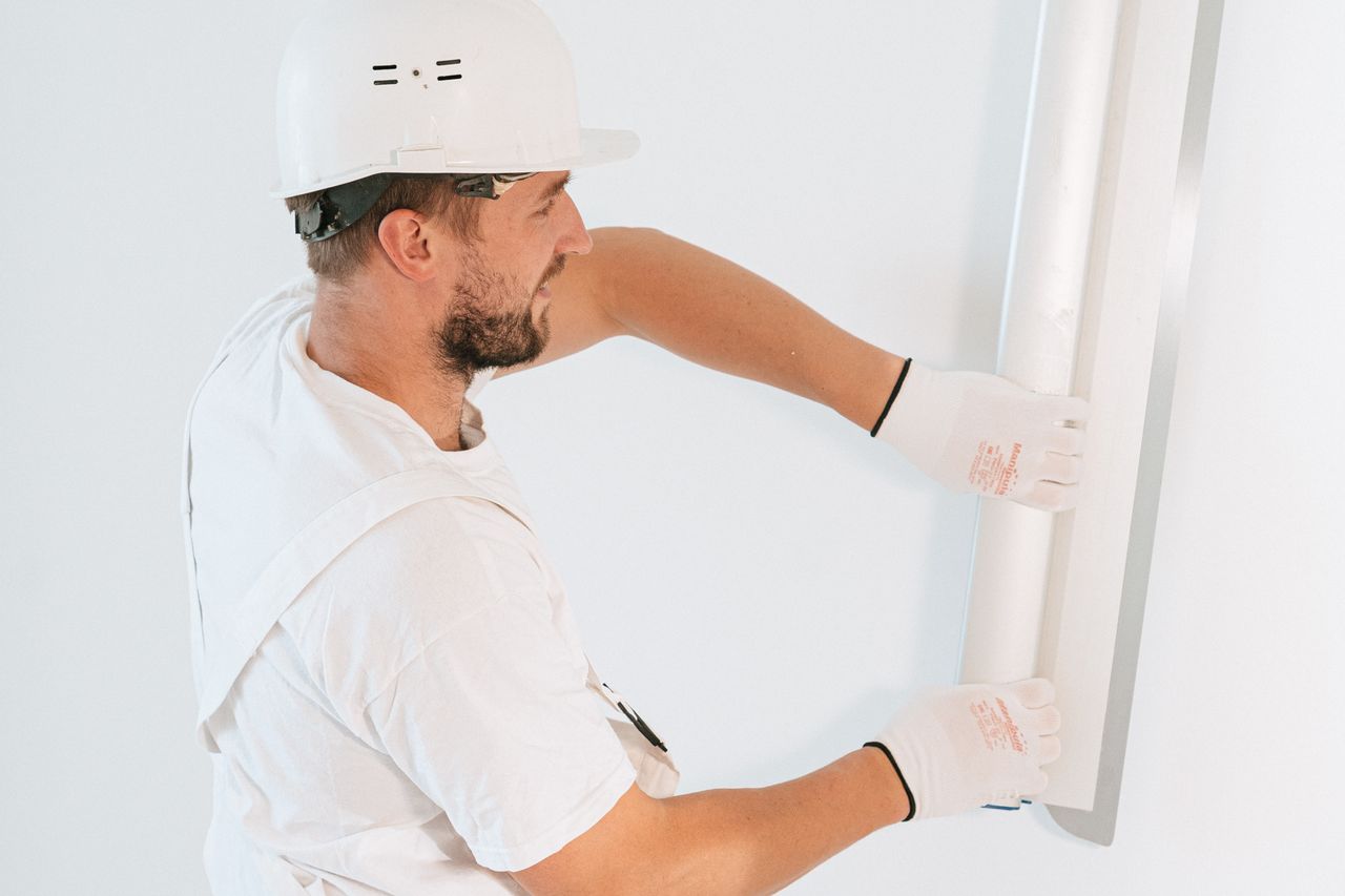 heros-img Professional construction worker installing drywall with gloves and helmet inside a building.